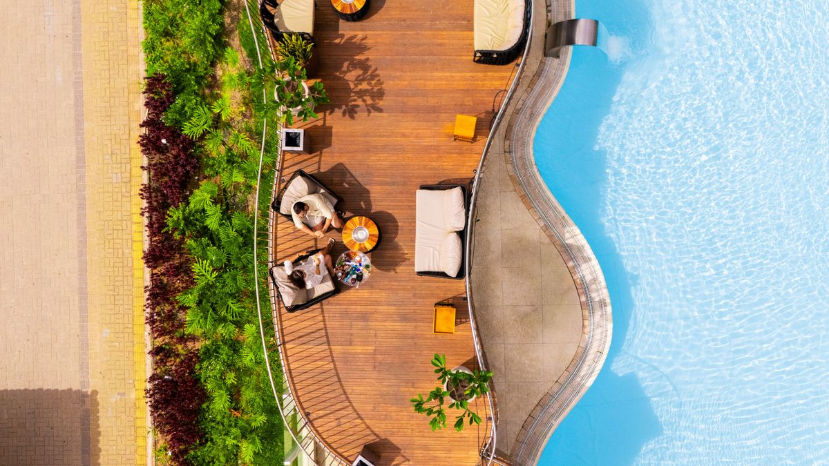 Deck e piscina do Esmeralda Praia Hotel vistos de cima, com área de descanso e jardinagem