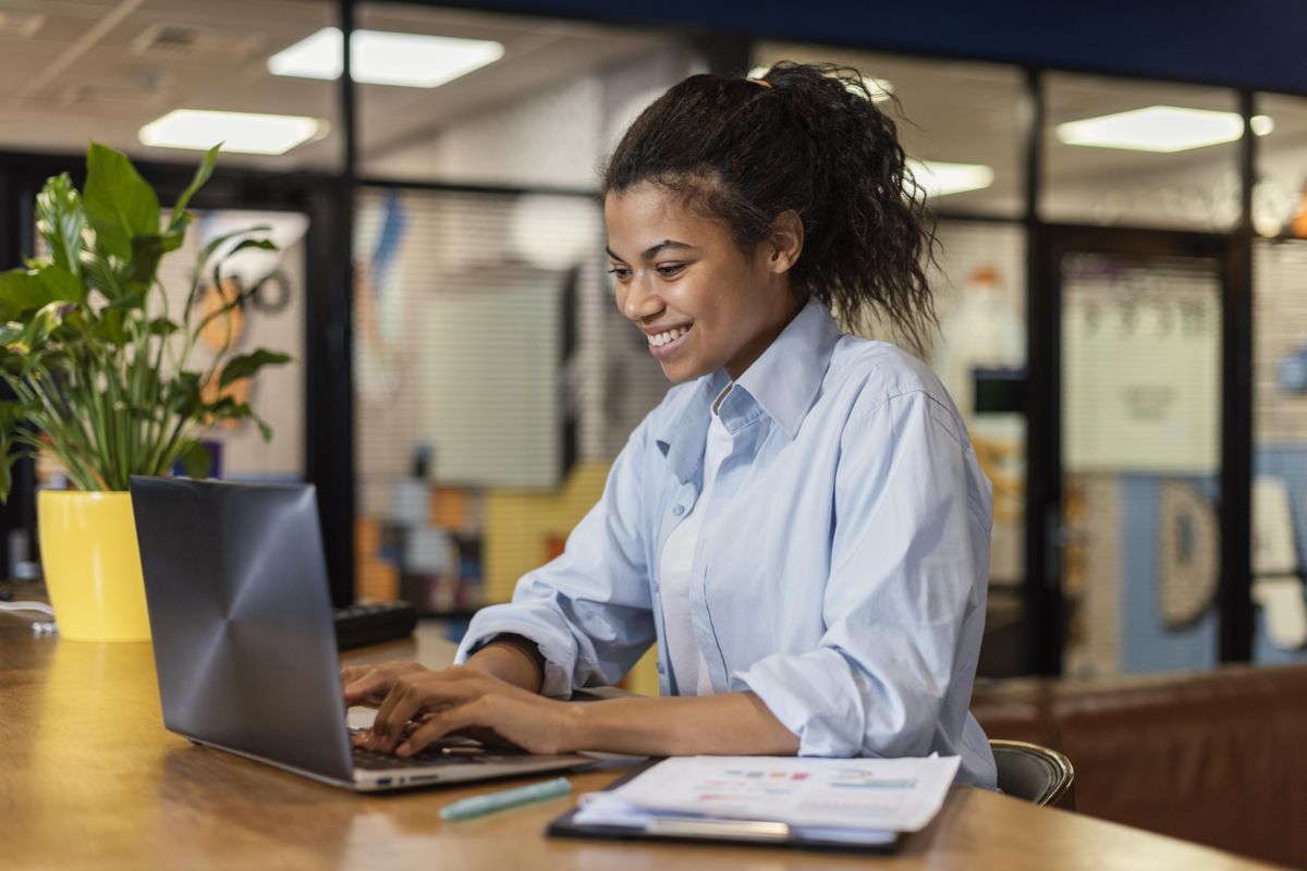 vista-lateral-de-uma-mulher-sorridente-trabalhando-com-um-laptop-no-escritorio.jpeg