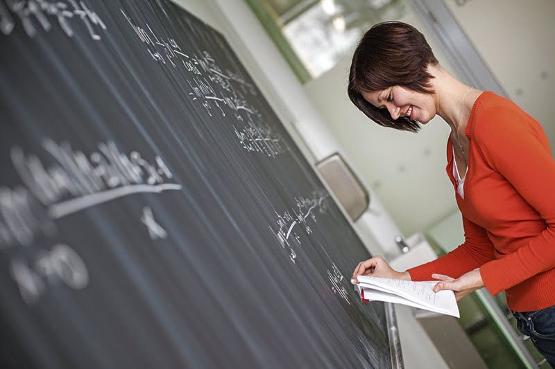 Pretty young college student/young teacher writing on the chalkb