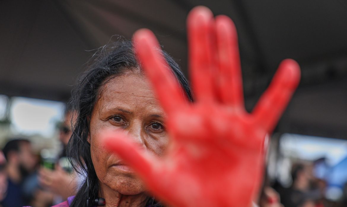 Mulher com a mão pintada de vermelho ergue o braço em ato de protesto contra a violência de gênero