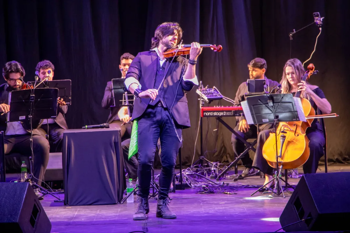 Violinista em apresentação acompanhado por músicos no palco