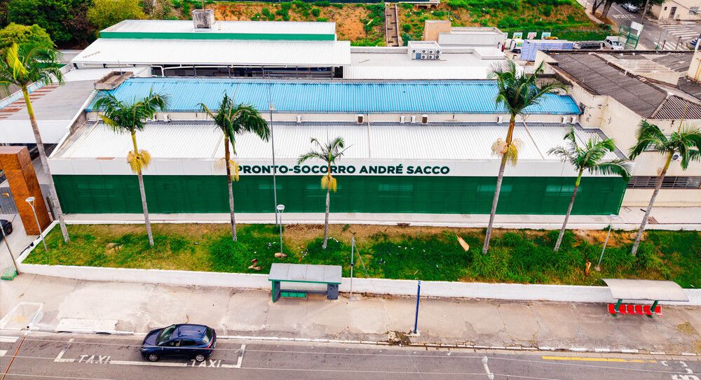 Vista aérea da fachada do Pronto-Socorro André Sacco, em Osasco, com letreiro verde e branco e palmeiras na calçada em frente ao prédio